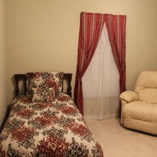 A cozy bedroom featuring a single bed with floral bedding, red curtains, and a comfortable armchair.