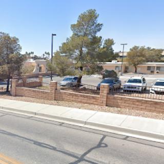 View of a parking lot near a school surrounded by trees and a fence.
