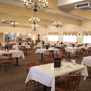 An empty restaurant dining room with white tablecloths and ornate chandeliers.