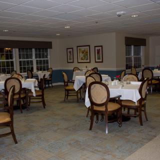 An empty dining room with neatly arranged tables and chairs, adorned with white tablecloths.