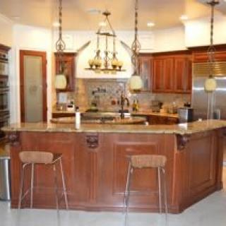 A modern kitchen with a central island and bar stools, featuring wooden cabinets and pendant lighting.