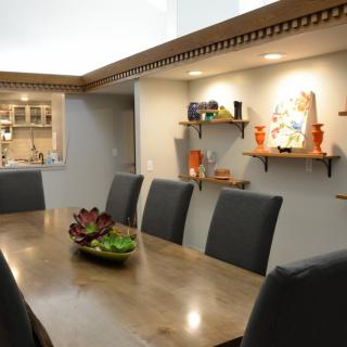 A modern dining room with a long wooden table, dark chairs, and decorative shelves displaying artwork and vases.