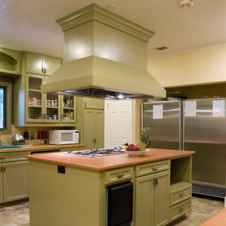 A modern kitchen with green cabinets, a central island with a stove, and stainless steel fridge.