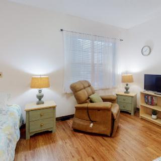 A cozy and well-lit living room featuring a recliner, bedside tables with lamps, and a television.