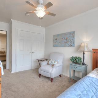 A cozy bedroom featuring a comfortable armchair, a bedside lamp, and a ceiling fan.