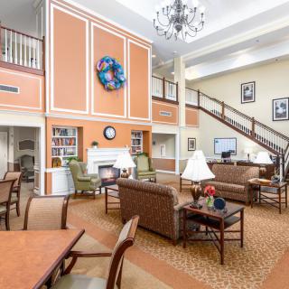 A spacious and cozy lounge area with comfortable seating, a large chandelier, and an elegant staircase.