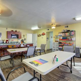 A bright and welcoming community room equipped for activities, featuring tables, chairs, and art supplies.