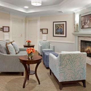 A cozy living room with sofas, chairs, a table, and a fireplace adorned with artwork.