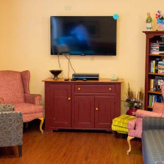 A cozy living room featuring a television mounted on the wall, a walnut cabinet, and comfortable armchairs.