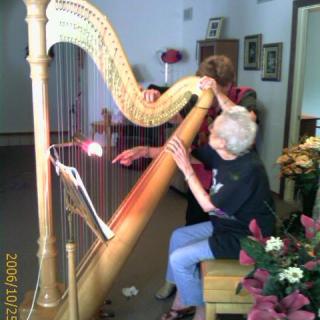 An elderly person receiving a harp lesson indoors.