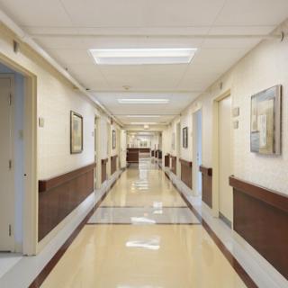 A well-lit hospital hallway featuring smooth flooring and framed artworks on the walls.