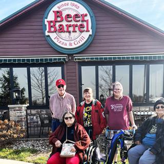A cheerful group gathered outside the Beer Barrel restaurant, enjoying a sunny day.