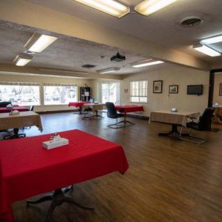 A spacious dining area with tables covered in red tablecloths and large windows providing natural light.