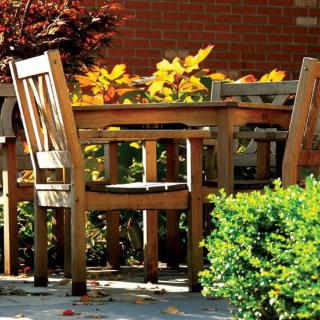 Wooden patio furniture set surrounded by lush garden plants.