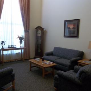 A cozy living room featuring a sofa set, coffee table, grandfather clock, and large window with curtains.