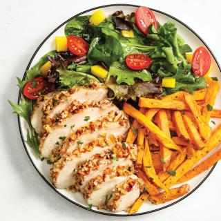 A healthy meal featuring sliced chicken, a fresh green salad with cherry tomatoes and yellow peppers, and a side of sweet potato fries.