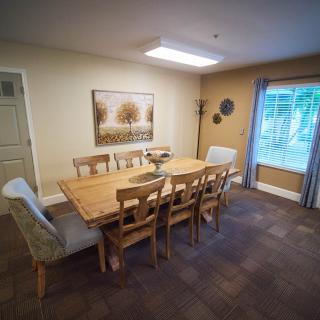 A cozy dining room with a wooden table set for eight, adorned with artwork and warm lighting.