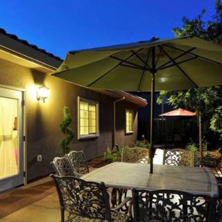 A cozy patio area with a table and umbrella set against the evening backdrop of a well-lit house exterior.
