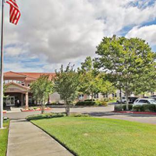 A building with a parking lot, surrounded by trees and under a cloudy sky, with a flagpole in front.