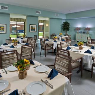 A spacious dining room with elegantly set tables and chairs, adorned with flowers and neatly folded napkins.