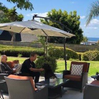 A sunny day on the patio with people relaxing under an umbrella.