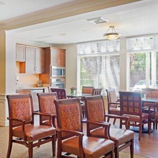 A cozy dining area with wooden chairs and a table, adjacent to a kitchen with modern appliances.