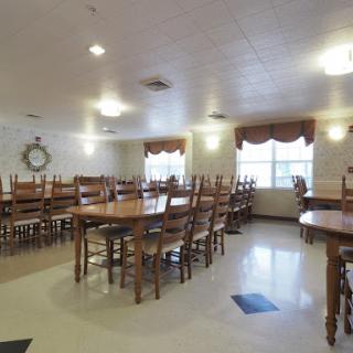 A spacious and well-lit dining room featuring wooden tables and chairs, designed for communal dining.