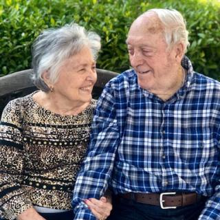 An elderly couple enjoys a joyful moment together outdoors.
