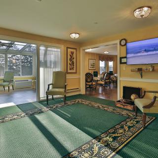 A cozy living room with a television, chairs, and large windows allowing natural light.