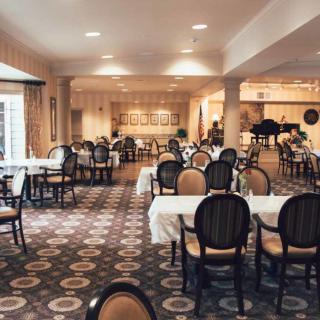 Elegant dining room with arranged tables and chairs, featuring warm lighting and a decorative carpet.