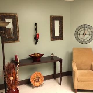 A cozy corner of a room featuring a light green wall, decorative frames, a stylish lamp, and elegant furniture.