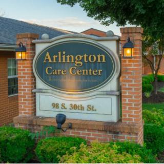 Sign for Arlington Care Center on a brick post with lights.