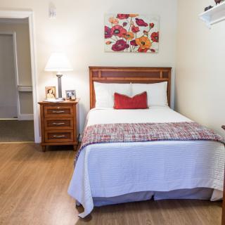A cozy bedroom with a neatly made bed, nightstand, and floral wall art.