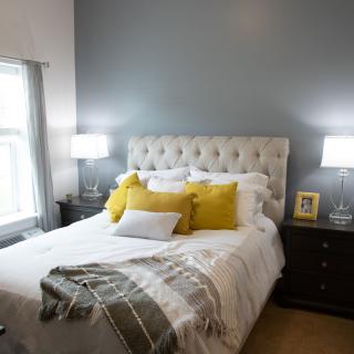 A cozy bedroom with a tufted headboard, yellow accent pillows, and matching lamps on dark nightstands.