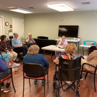 A group of seniors engaged in a community meeting inside a room.