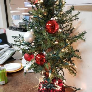 A festive miniature Christmas tree adorned with red and white ornaments, bringing holiday cheer to the office.