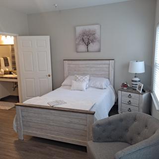 Cozy bedroom with white decor, featuring a bed, nightstand, and a comfortable armchair.