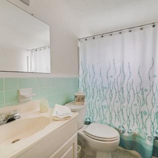 A clean bathroom with green tiles, featuring a sink, toilet, and a decorative shower curtain.