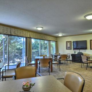 A spacious dining room with multiple tables and chairs, featuring large windows and a television.