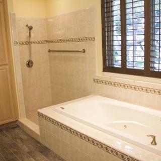 A modern bathroom featuring a bathtub, shower area, and window with blinds.