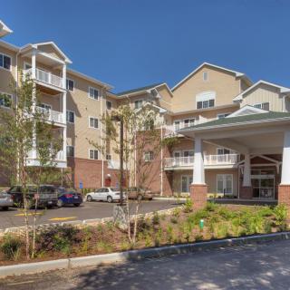 A modern apartment complex with multiple levels, landscaped surroundings, and a parking area.