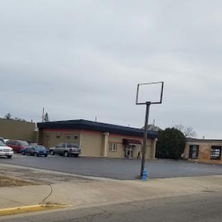 An empty basketball hoop stands near a building on a cloudy day.