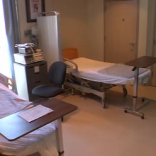A view of a hospital room with a bed, chair, and medical equipment.