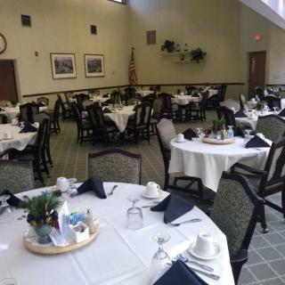 A dining area with tables set for a meal, featuring white tablecloths and black napkins.