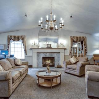 A cozy living room with comfortable sofas, a central coffee table, and a chandelier illuminating the space. The fireplace adds warmth, while elegant curtains frame the windows.