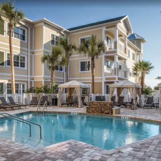 A luxurious resort with a sparkling outdoor pool surrounded by palm trees and elegant buildings.