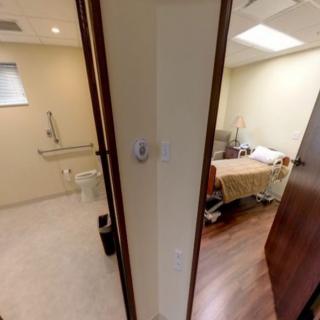 View of a hospital room with an adjoining bathroom, featuring a bed and clean surroundings.