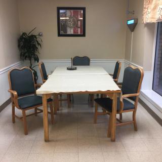 A simple dining area with a table and six chairs, decorated with a plant and wall art.