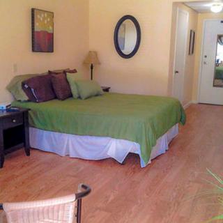 A cozy bedroom with green bedding, wooden flooring, and simple decor.
