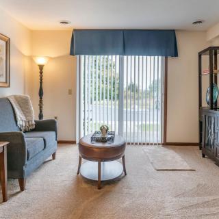 A cozy living room with a sofa, coffee table, lamp, and large window with vertical blinds.